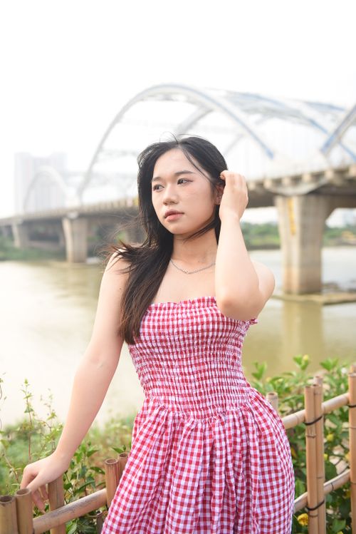 Free Woman in a red checked dress poses by the river with a bridge in the background. Stock Photo