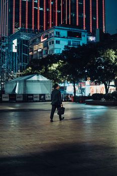 A solitary businessman walks through the vibrant streets of Ho Chi Minh City at night.