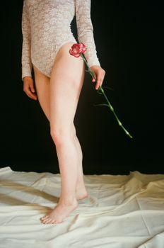 Artistic photo of a woman in a lace bodysuit holding a pink flower against a dark backdrop.