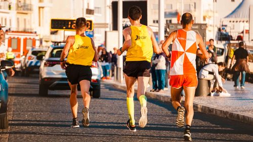 Free Three athletes running in a city marathon on a sunny day, showcasing endurance and motion. Stock Photo