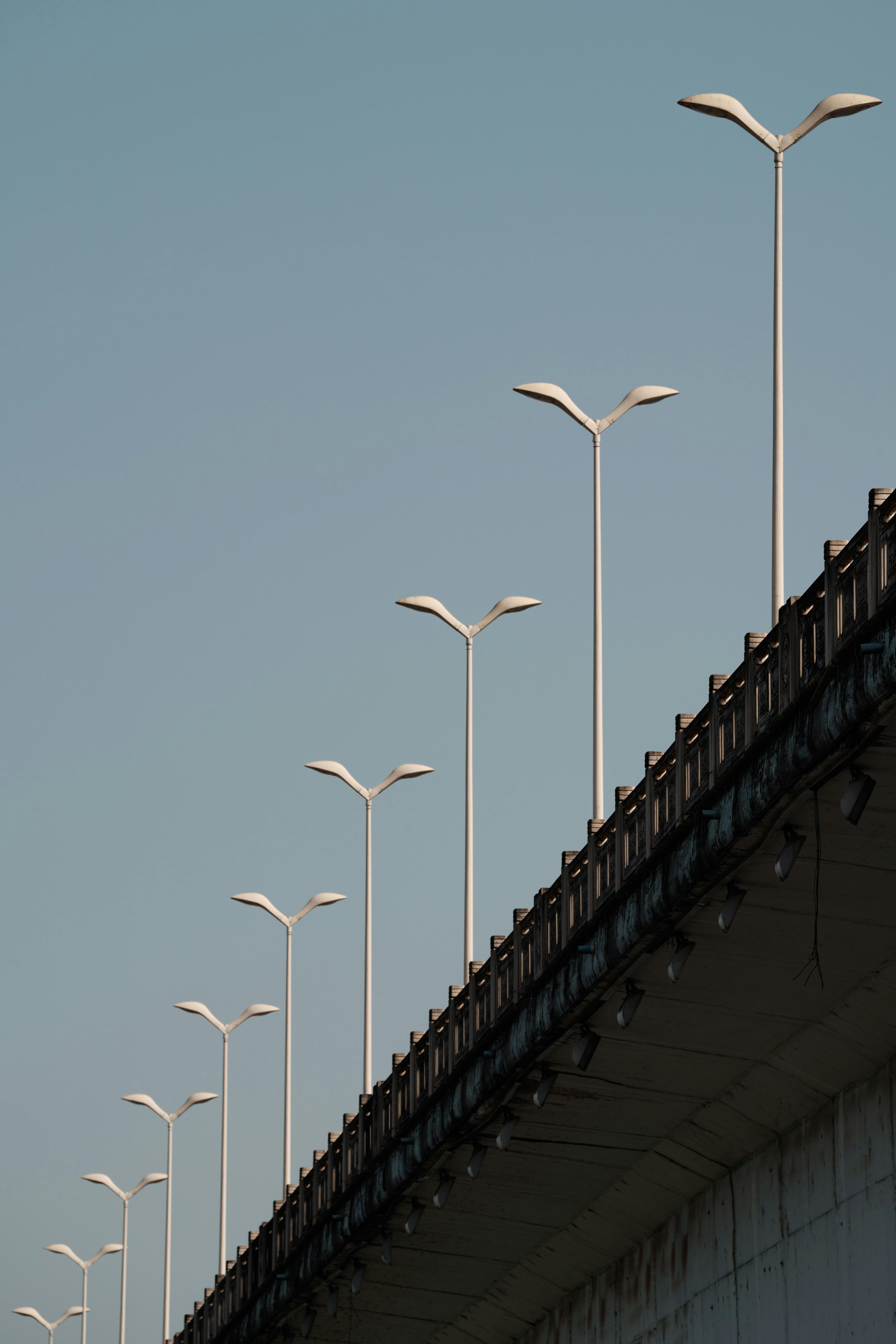 Minimalist view of an overpass with futuristic streetlights against a clear blue sky.
