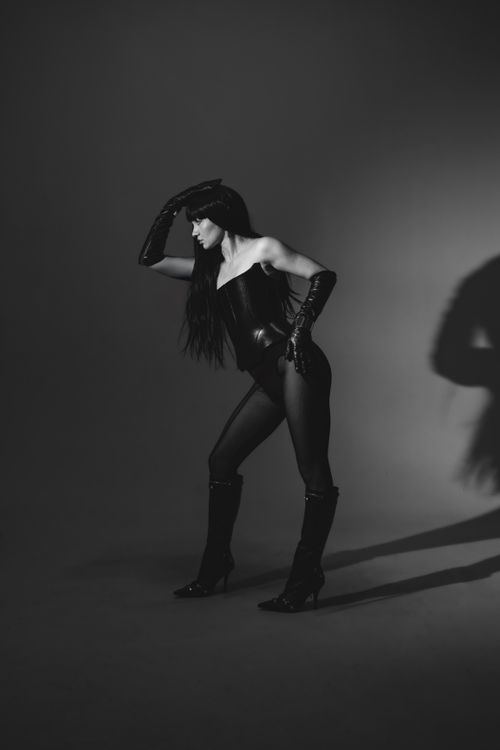 Free Elegant black and white portrait of a woman posing in a studio setting wearing a black outfit and high heel boots. Stock Photo