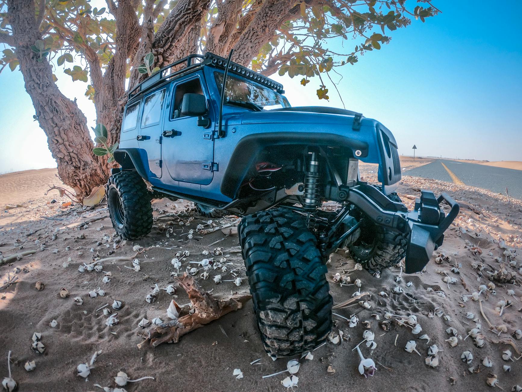 Blue off-road vehicle parked under a tree in the sandy desert of Dubai, showcasing rugged suspension.
