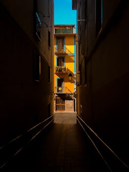 明亮的黄色建筑被黑暗的城市小巷包围，阳光与阴影交织，形成鲜明对比