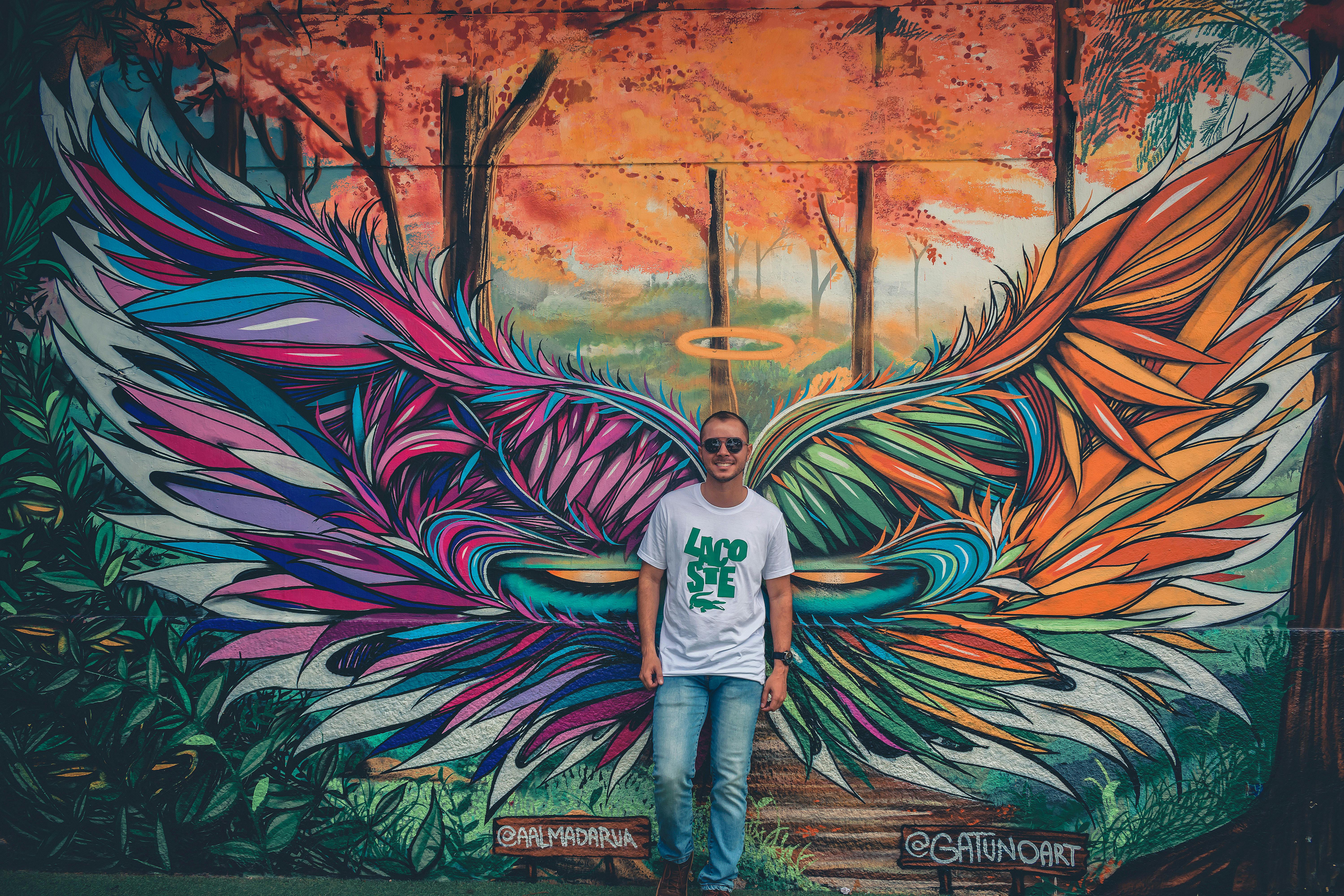 Man Wearing White And Green Crew Neck Shirt Leaning On Graffiti Wall Art Free Stock Photo