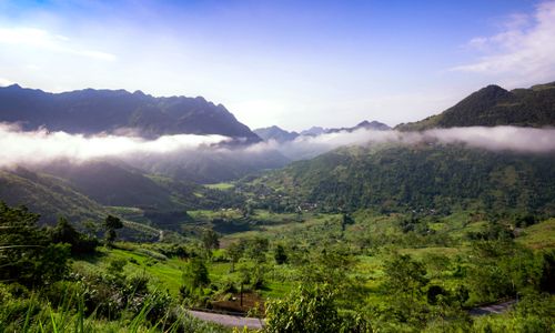 Free Scenic mountain valley landscape with mist and lush greenery under a clear blue sky. Stock Photo