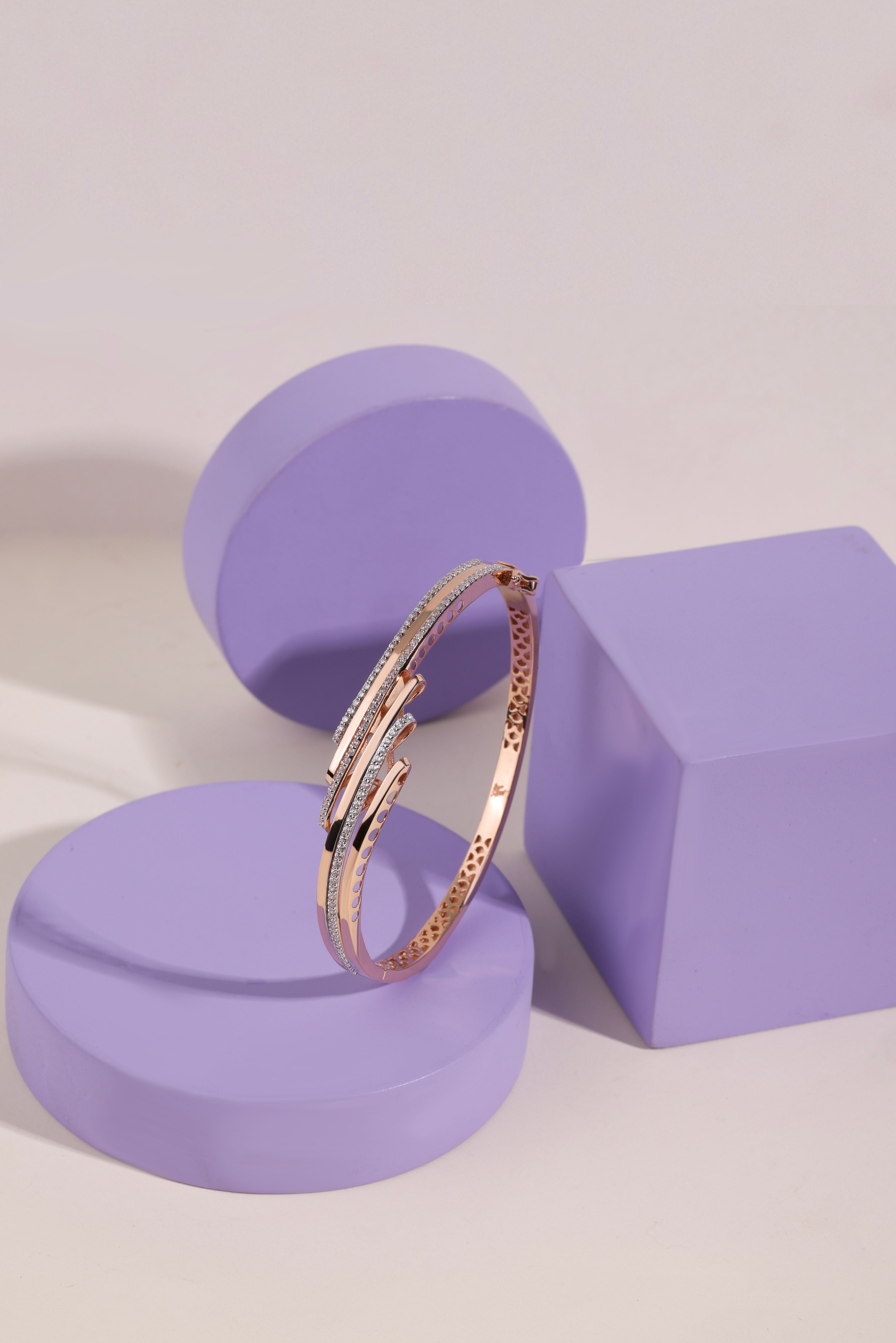Uma imagem de close-up de uma pulseira elegante em ouro rosa exibida em um suporte pedestal moderno em tom de malva.