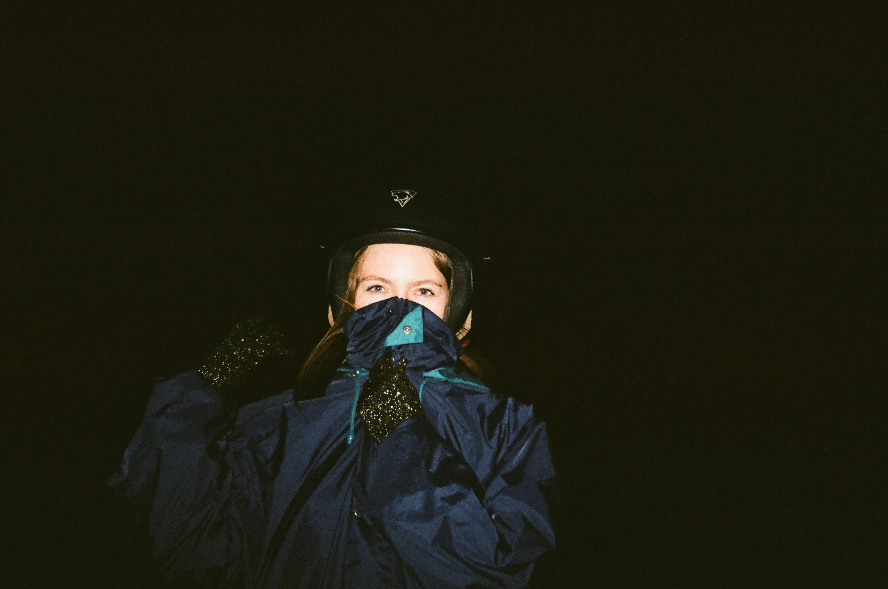 A woman in a dark jacket and helmet, with a covered face, captured at night.