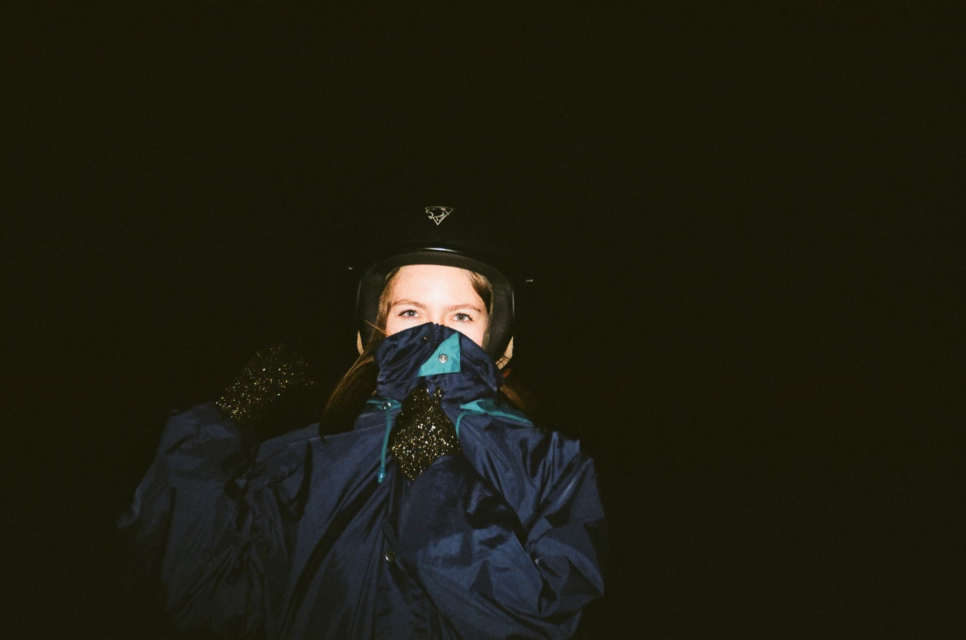 A woman in a dark jacket and helmet, with a covered face, captured at night.