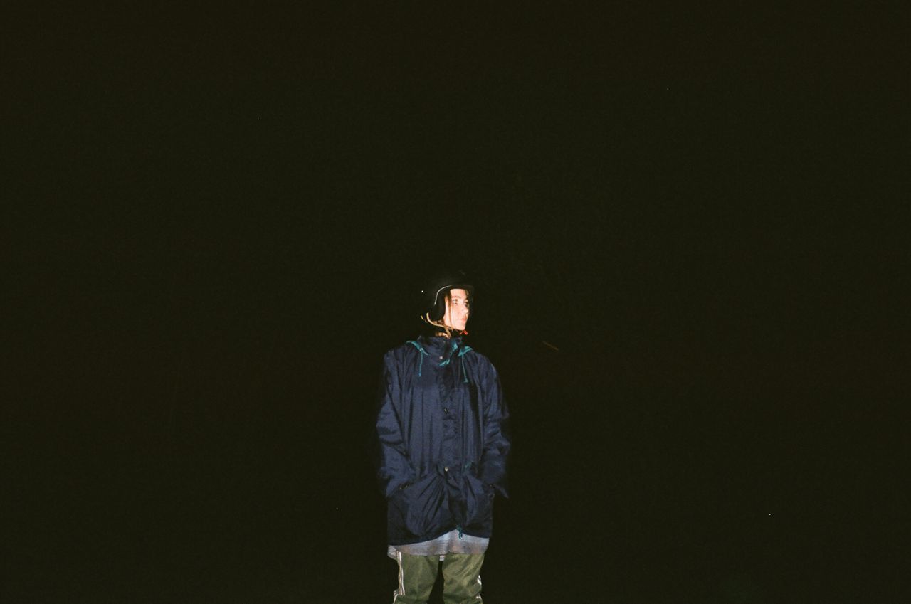a solitary figure in a dark jacket stands against a black background i