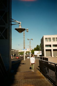 一位孤独的女人走在阳光明媚的城市街道上，两旁是现代建筑