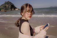 亚洲女子拿着智能手机在海滩上享受阳光明媚的一天