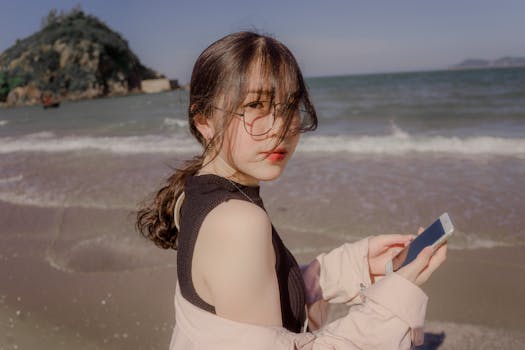 一位亚洲女子在海滩上拿着智能手机，享受着阳光明媚的一天