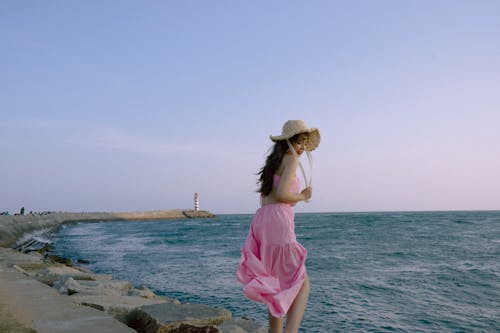 A woman in a pink dress is walking along the edge of the water