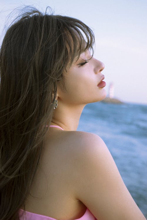 A woman with long hair and earrings looking at the ocean