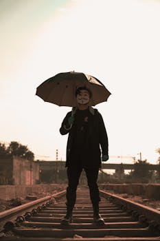 Mysterious figure with an umbrella on railway tracks, evoking intrigue and anonymity.