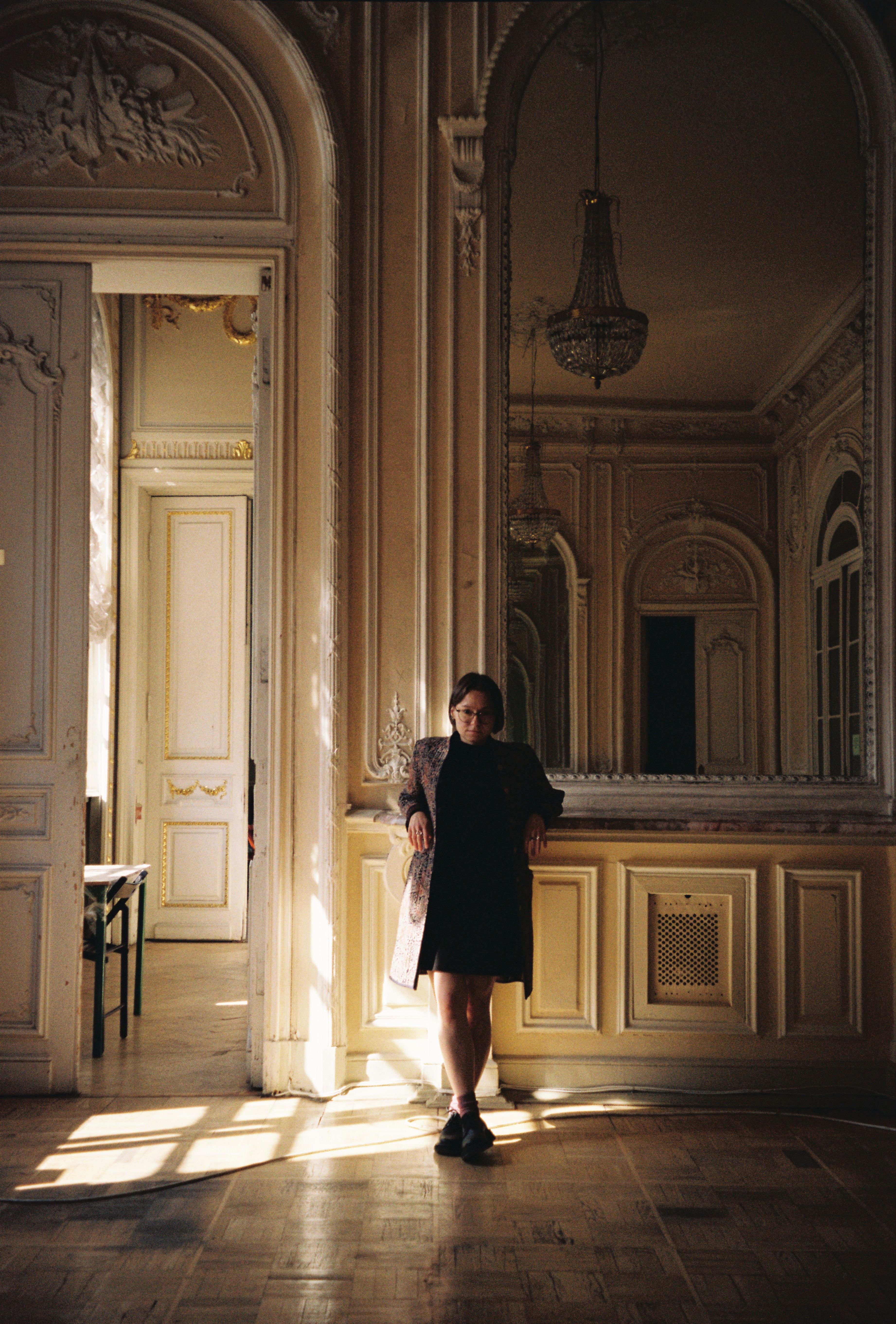 A woman stands gracefully in a vintage ornate room with warm lighting.