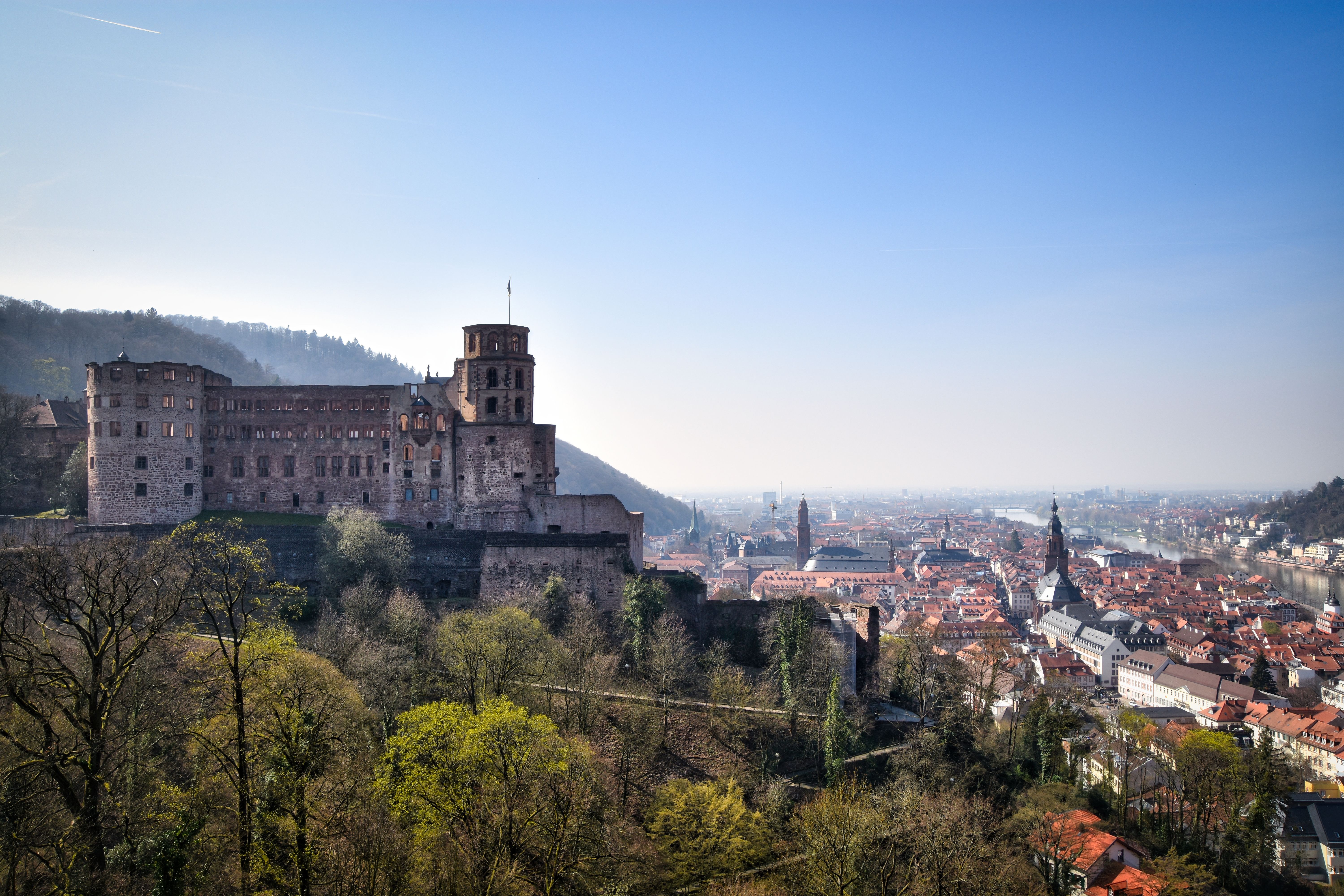 A panoramic view of a European city with a castle on a hill, a river, and colorful buildings under blue sky