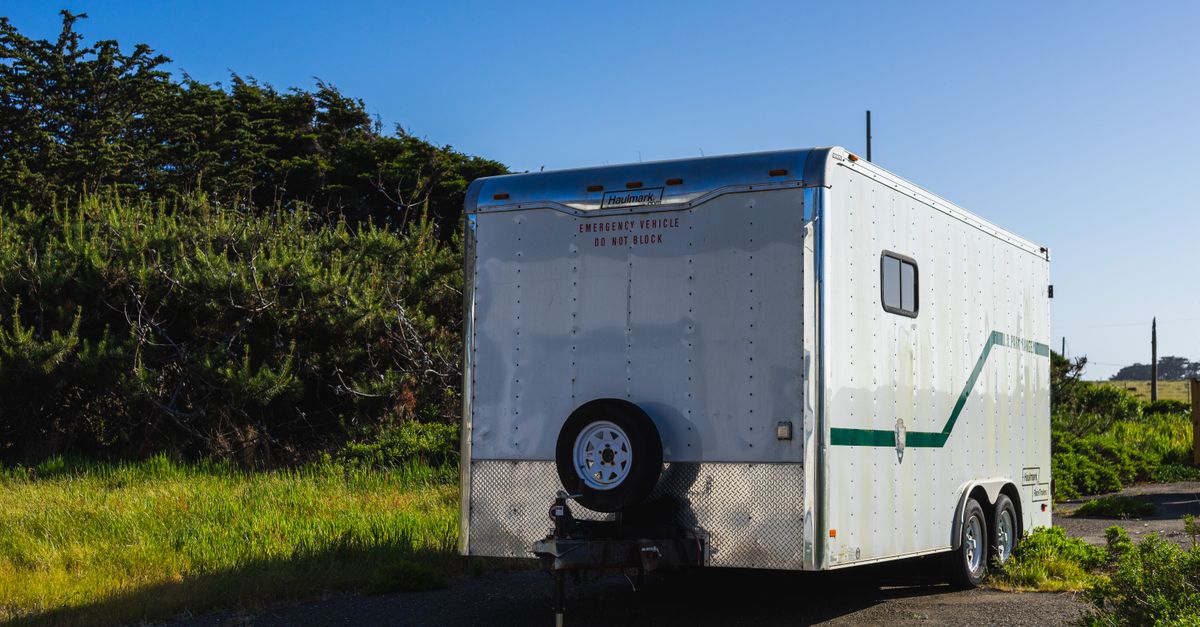 A parked white trailer surrounded by greenery under a clear blue sky in a rural area.
