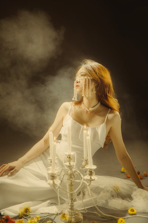 A woman in white dress sitting on the floor with candles