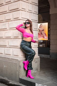 Stylish woman in pink and black fashion outfit posing against a wall in an urban setting.