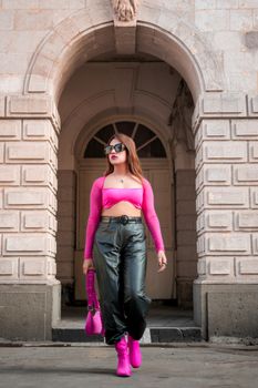Young woman in stylish black pants and pink top walking confidently outdoors.