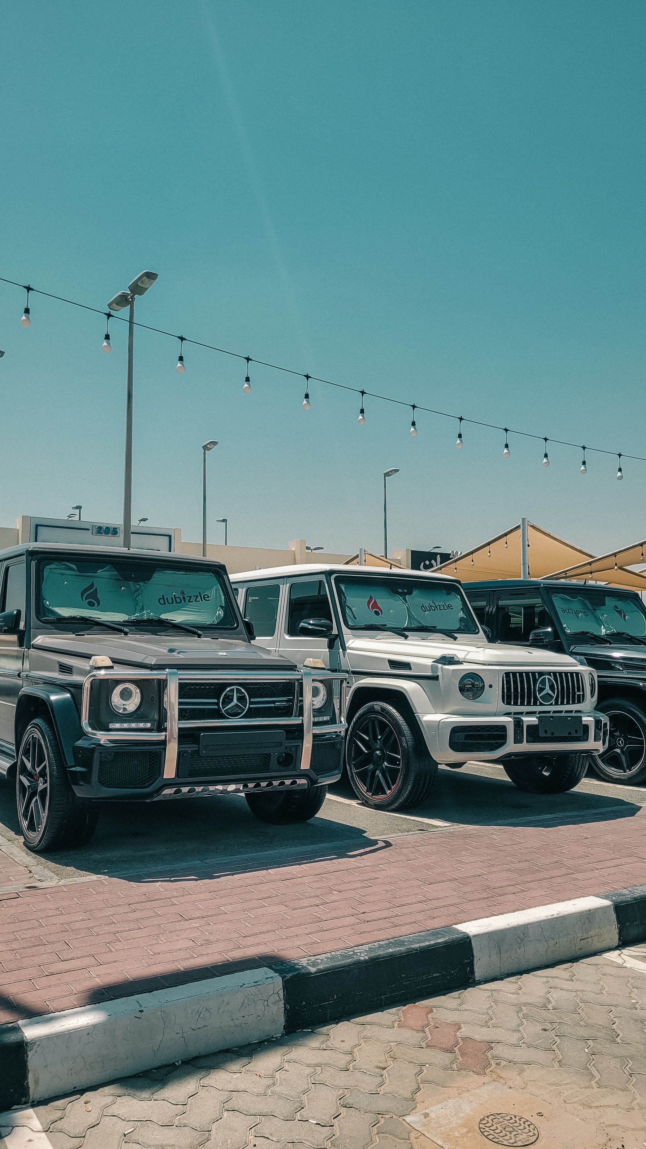 A lineup of luxury Mercedes-Benz G-Class SUVs parked outdoors in a sunny urban setting.