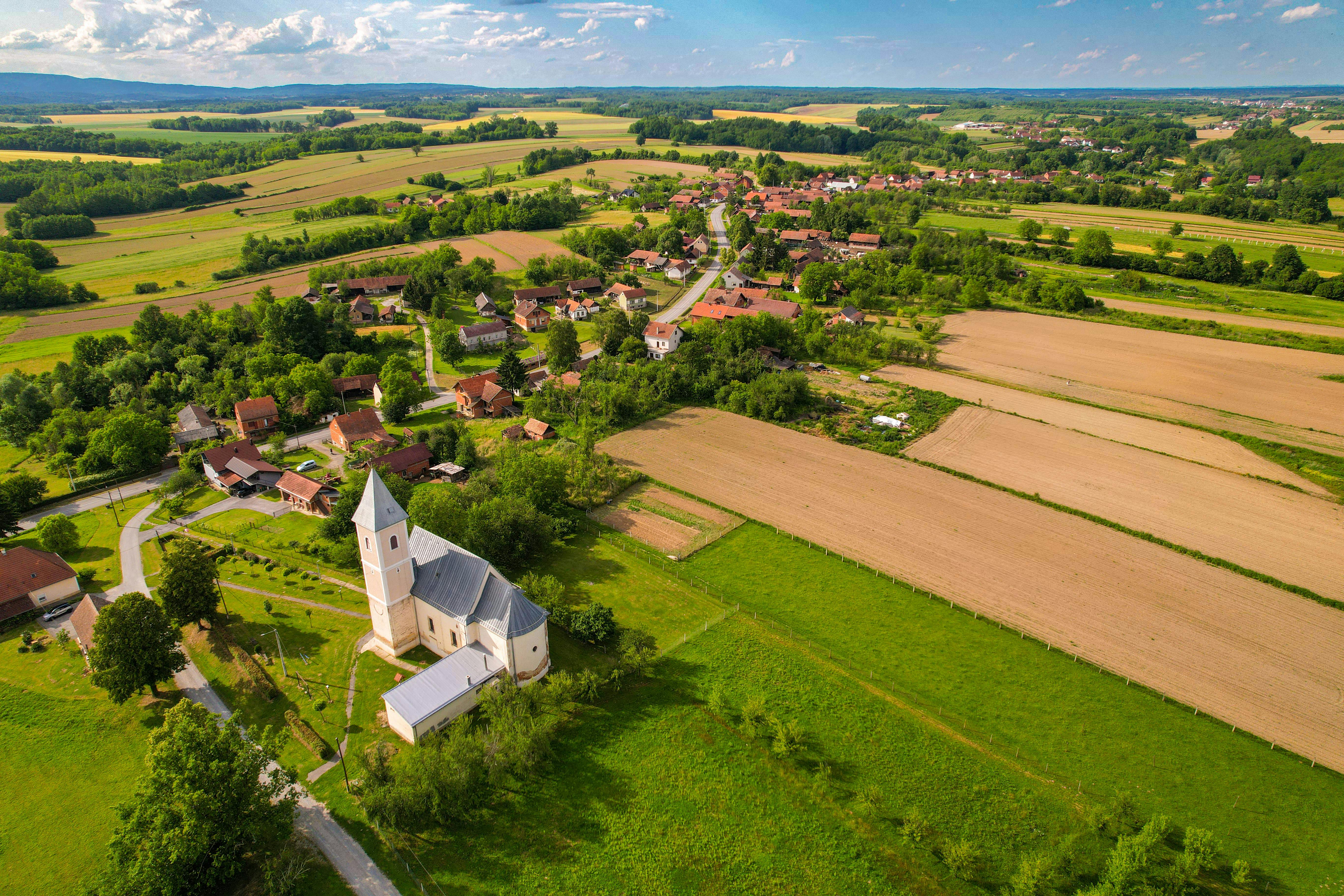 Aerial view of a rural village with a church, surrounded by farmland, fields and patches of woodland