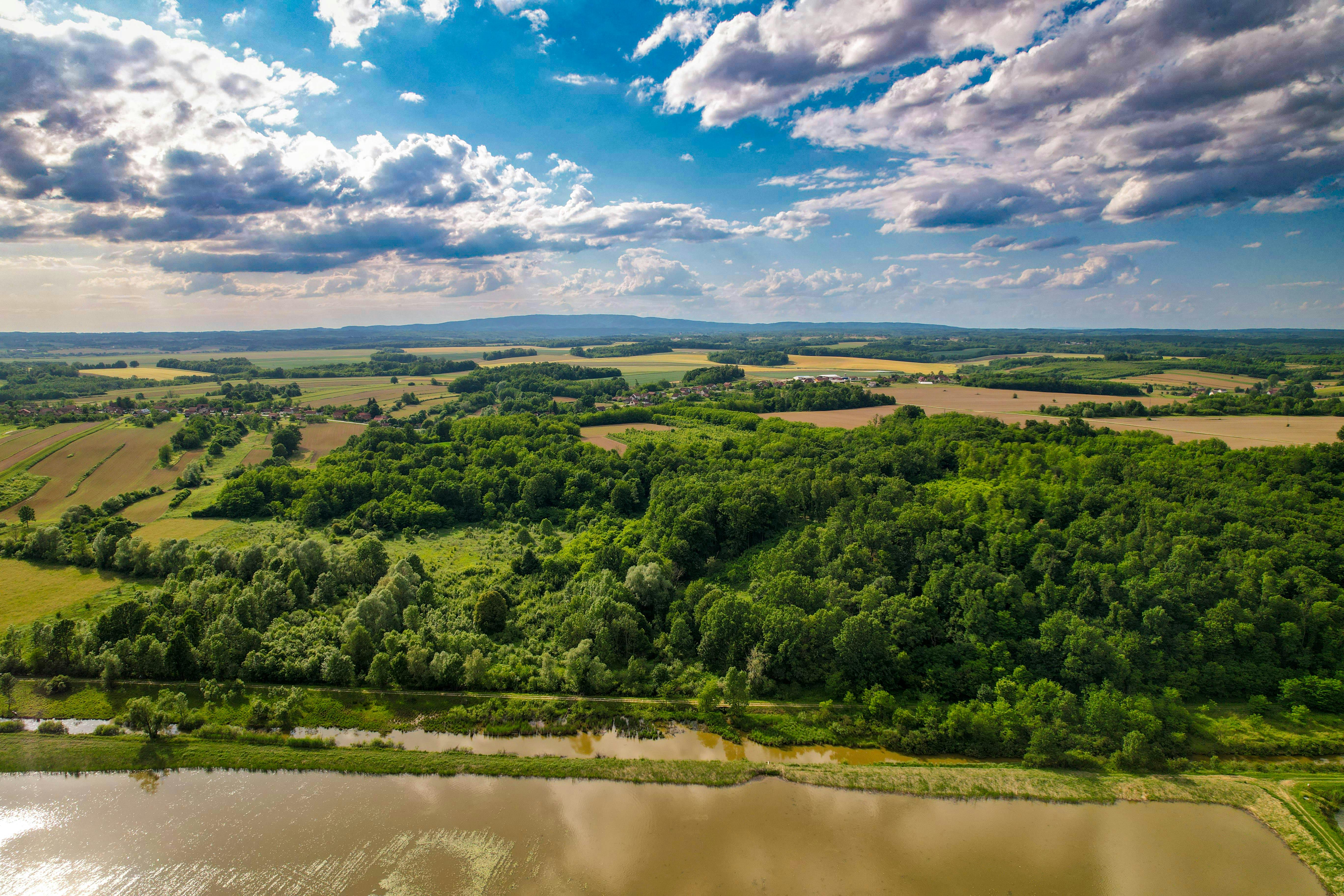 Aerial view of lush green landscape and fields in Kaniška Iva, Croatia, under a vibrant sky.