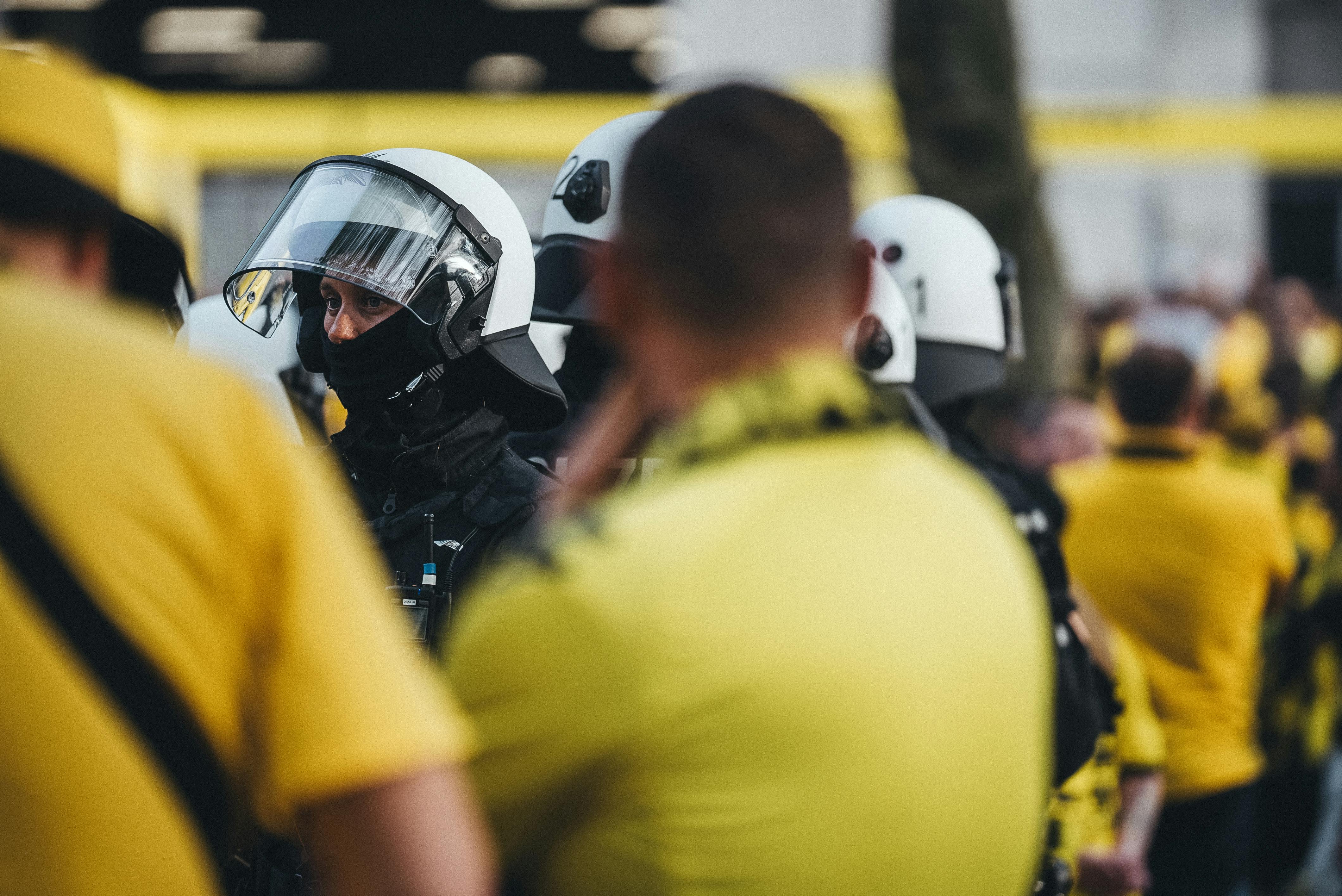 Police officer in protective gear during a public demonstration with crowd in background.