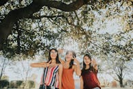 三个女人在阳光明媚的树下笑着摆姿势，享受户外乐趣