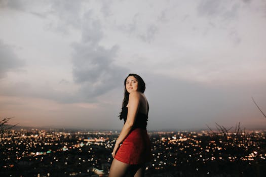 黄昏时分，一名年轻女子站在山上，俯瞰着城市灯火与宁静夜空融为一体的景象