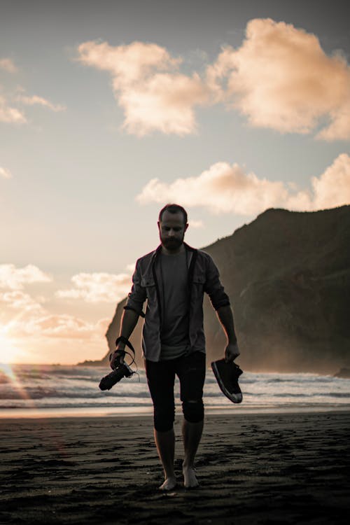 Homem Segurando Sapatos E Câmera Andando Na Praia