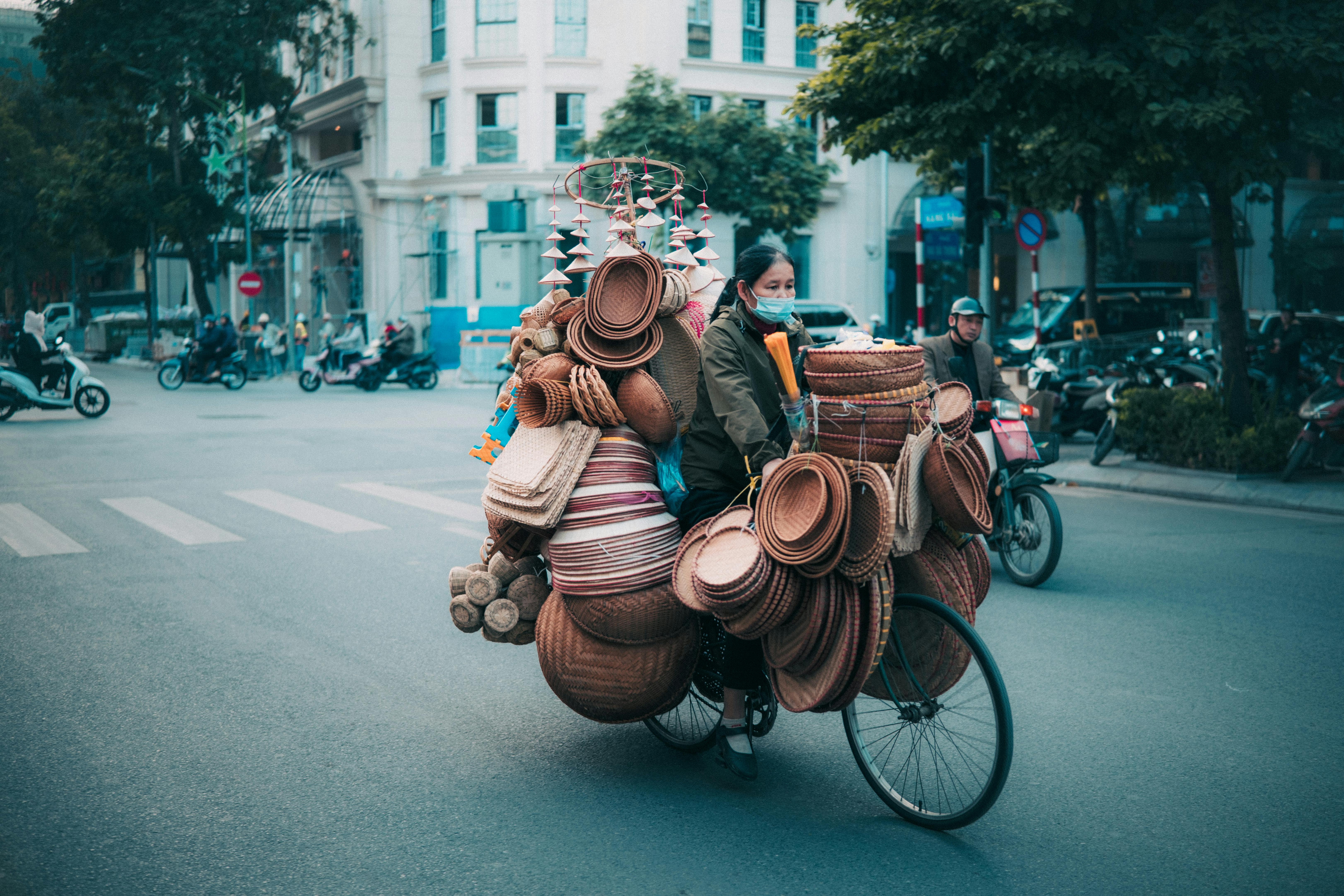 Free Woman cycling through city streets carrying a load of wicker baskets. Stock Photo