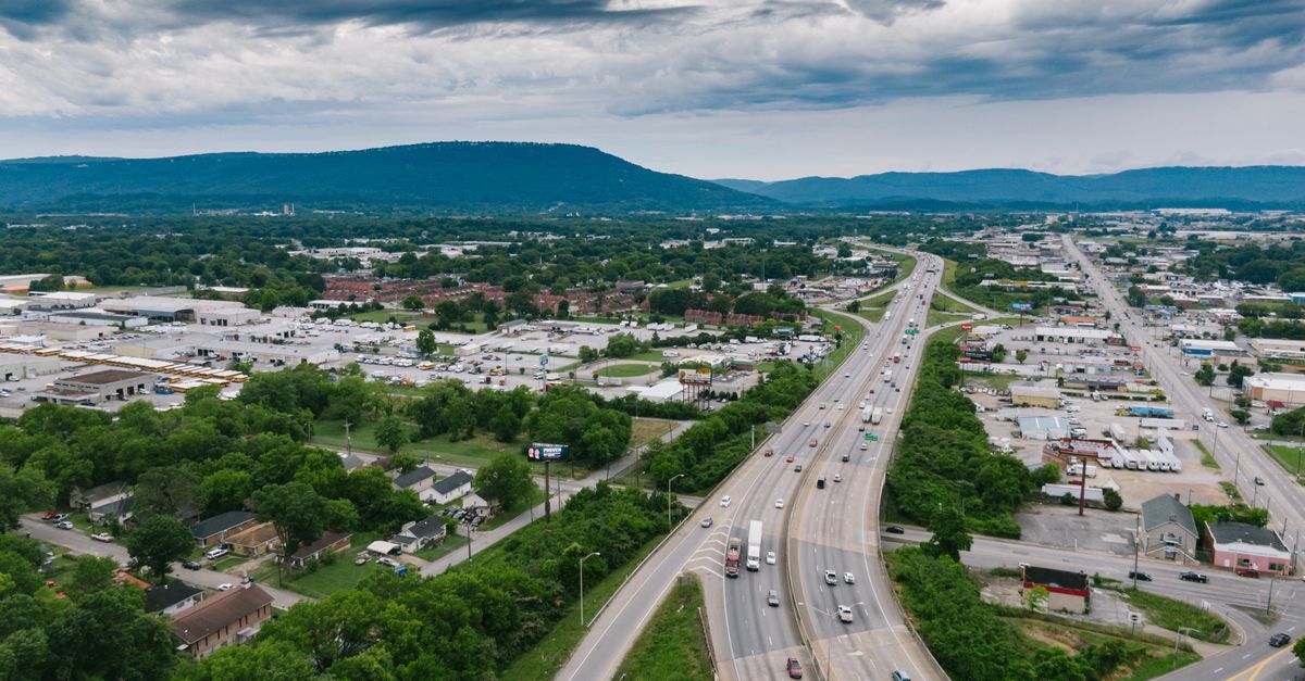Aerial view of a busy highway in Chattanooga with lush greenery and urban landscape under cloudy skies.