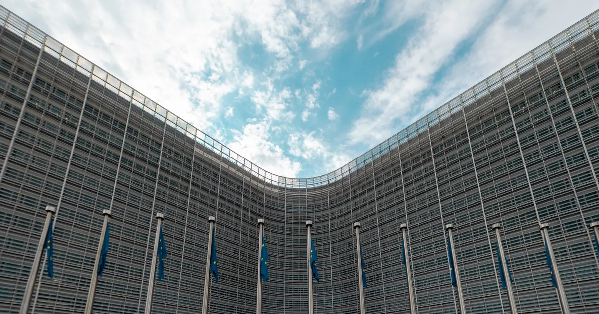 The curved glass-and-steel facade of a large office building with flags along its base under a cloudy sky, representing product liability standards and the burden of proof for AI system defects