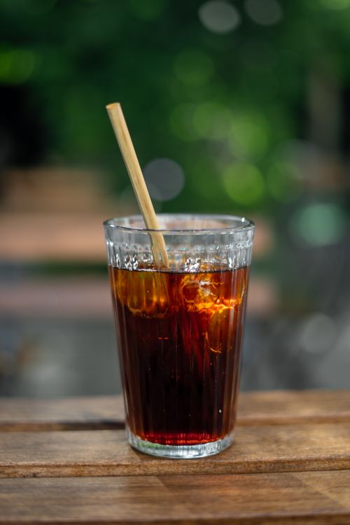 Free Iced coffee served in a clear glass with a bamboo straw on a wooden table, perfect refreshment. Stock Photo