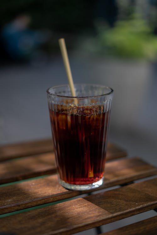 A glass of cola with a straw on a wooden table