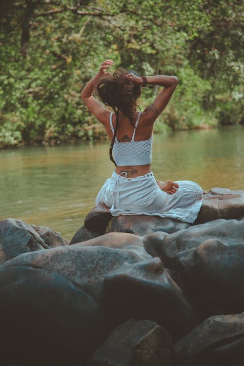 бесплатная Фотография женщины, сидящей на скале у реки Стоковое фото