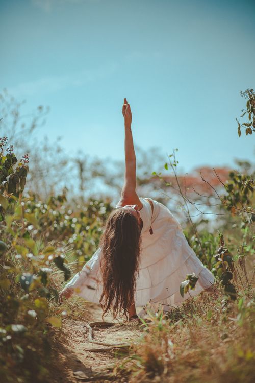 Free A woman practicing yoga outdoors in a white dress, surrounded by nature and sunlight, embodying serenity and focus. Stock Photo