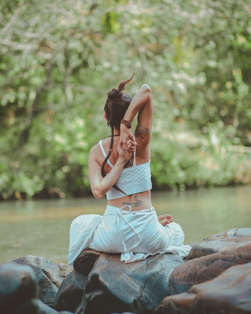 Back view photo of a woman sitting near body of water doing yoga