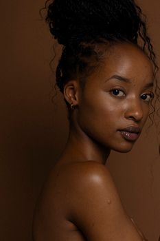 Captivating studio portrait of a woman with natural makeup and styled hair against a brown backdrop.