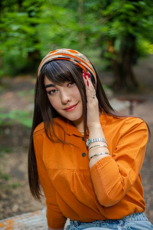 Free Portrait of a stylish woman in nature, wearing an orange shirt and accessories. Stock Photo