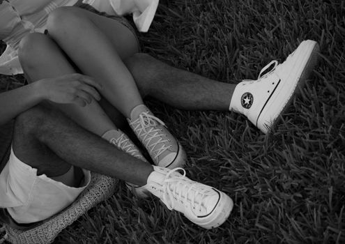 Black and white photo of a couple sitting on grass with Converse sneakers.