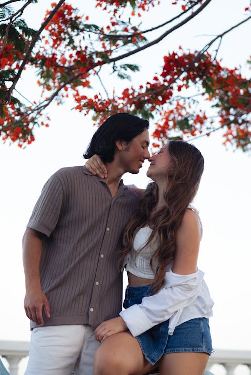 A couple kissing under a tree with red flowers
