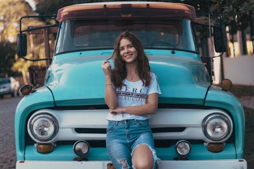 阳光明媚的户外，一位快乐的年轻女子在一辆经典复古卡车前摆姿势