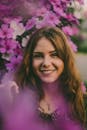 一位微笑的女人的肖像，背景是户外充满活力的紫色花朵