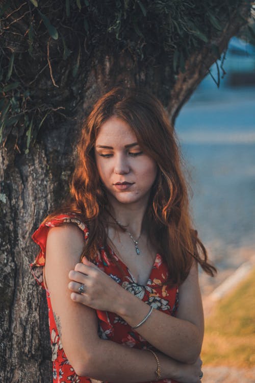 Woman Wearing Red Floral Top Leaning on Tree