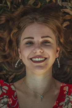 Close-up of a smiling woman lying on leaves, showcasing natural beauty and joy.