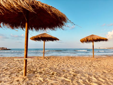 A tranquil beach scene in Gournes Gouvon, Greece with natural straw umbrellas and calm sea waves.